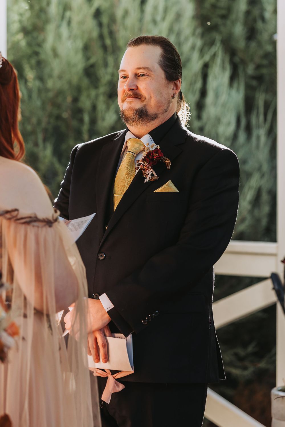 A person in a black suit and yellow tie stands emotionally during what appears to be a wedding ceremony.