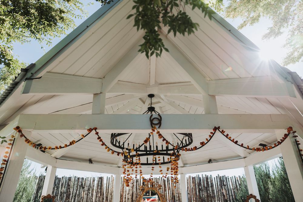 A white outdoor wedding pavilion decorated with string lights and floral garlands creates a romantic atmosphere.
