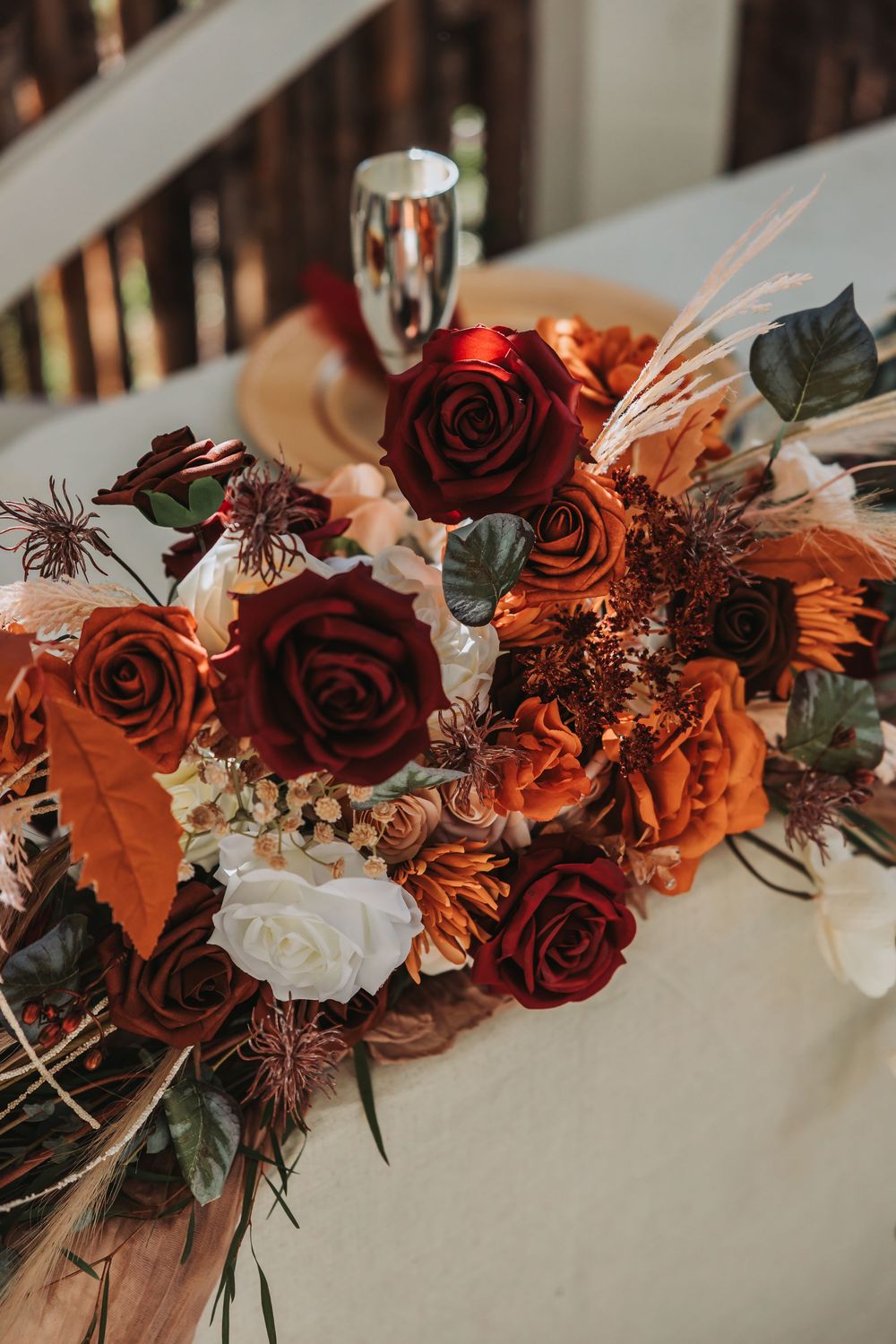 Close-up view of dark red roses and orange flowers arranged in an elegant autumn wedding floral arrangement.