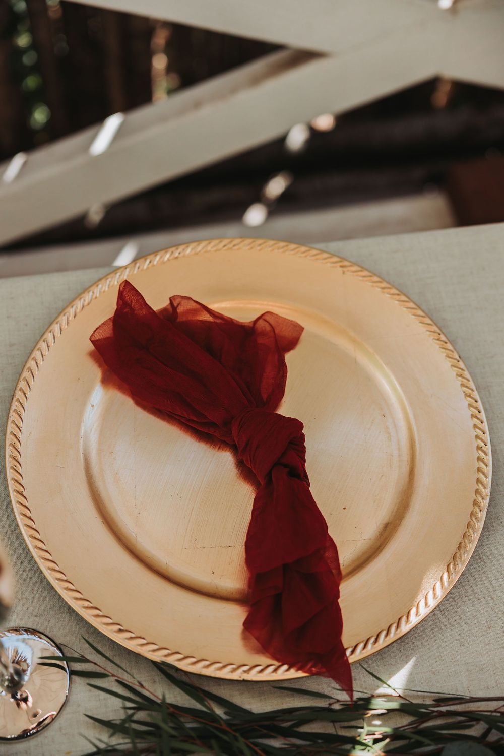 A cream-colored plate with a burgundy napkin elegantly folded on a gray tablecloth with holiday decorations.