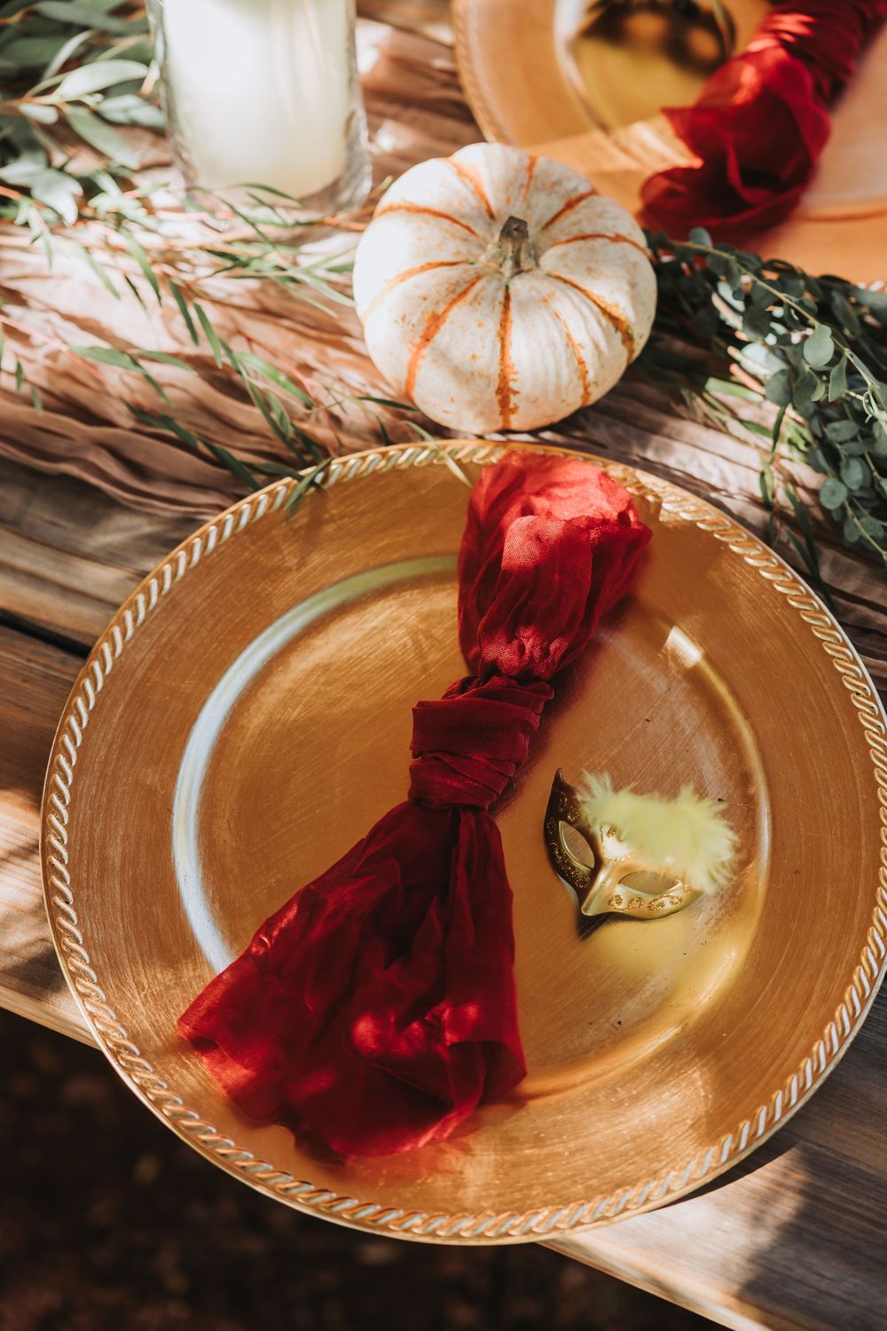 A gold decorative plate with a red velvet ribbon and white pumpkin decor creates an elegant autumn table setting.
