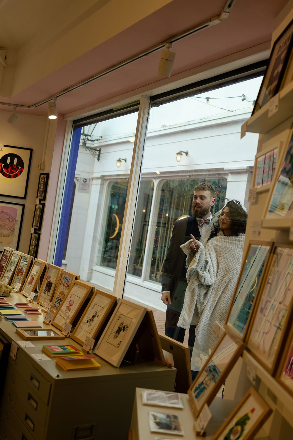 Art gallery interior showing framed artwork displayed along white walls with natural lighting from windows.