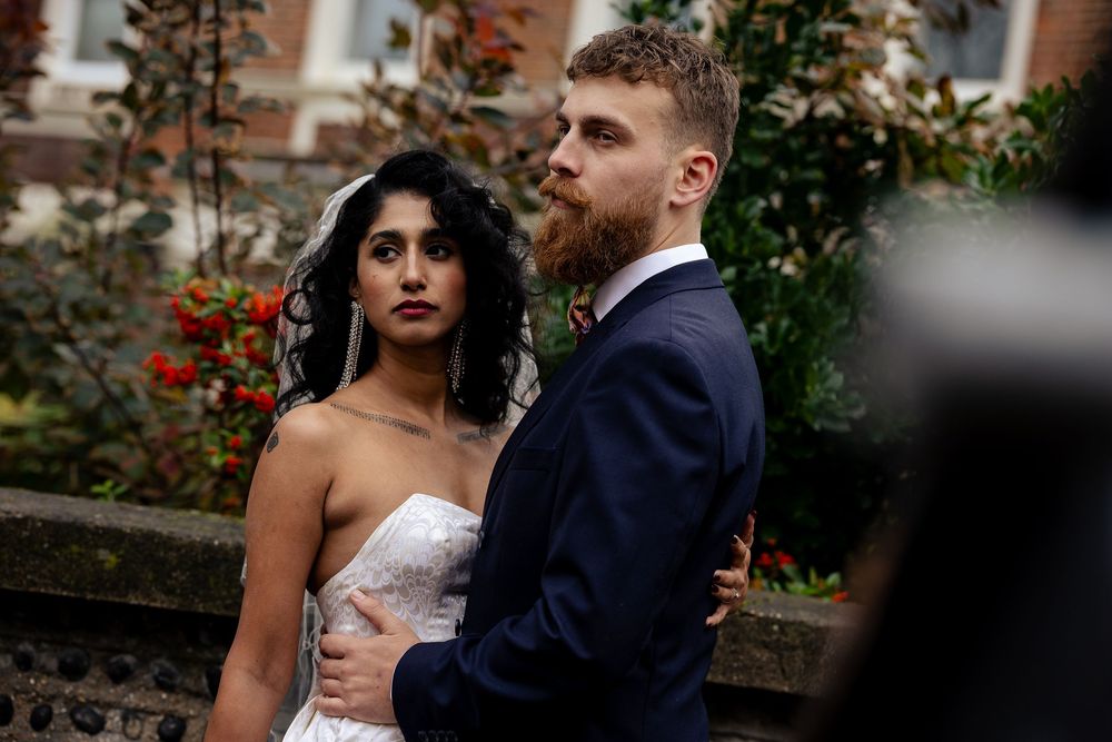 Romantic wedding couple poses together in a garden with red flowers in the background.