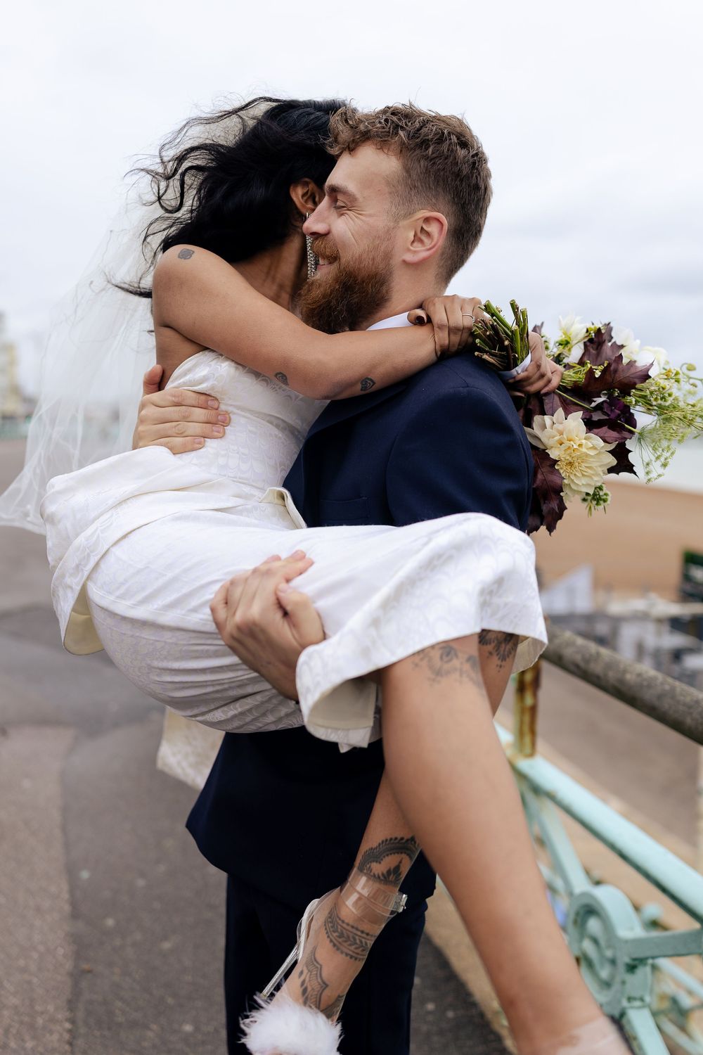 Playful wedding couple shares joyful embrace on urban rooftop with bride's dress flowing.