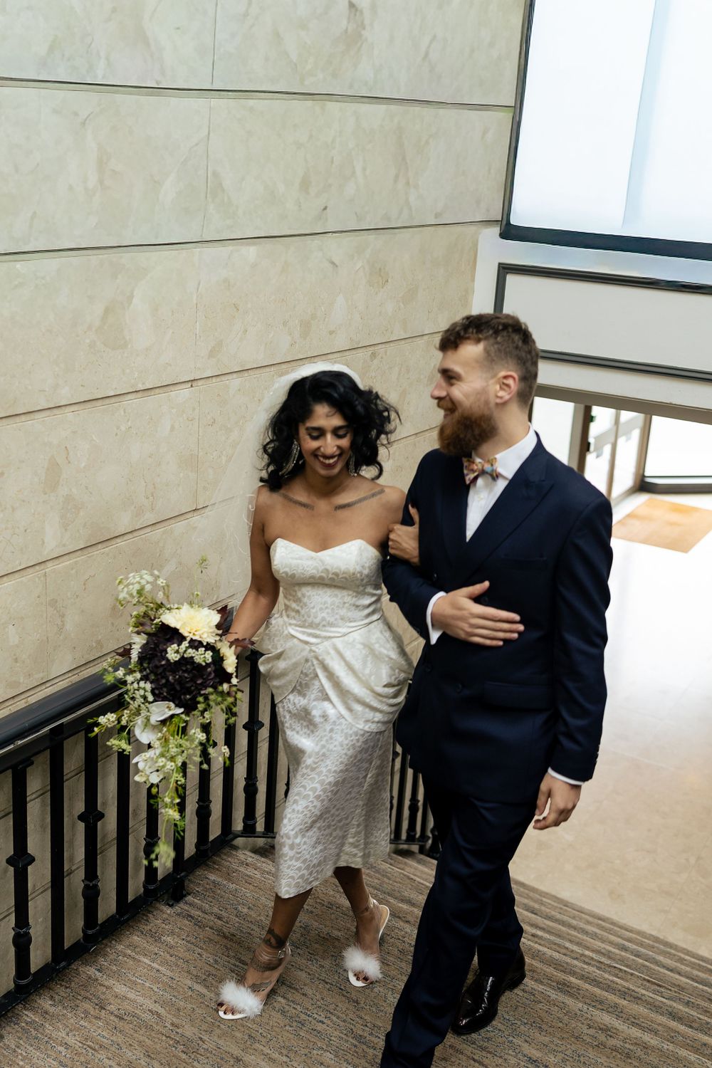Couple in wedding attire playfully walking down a hallway together.