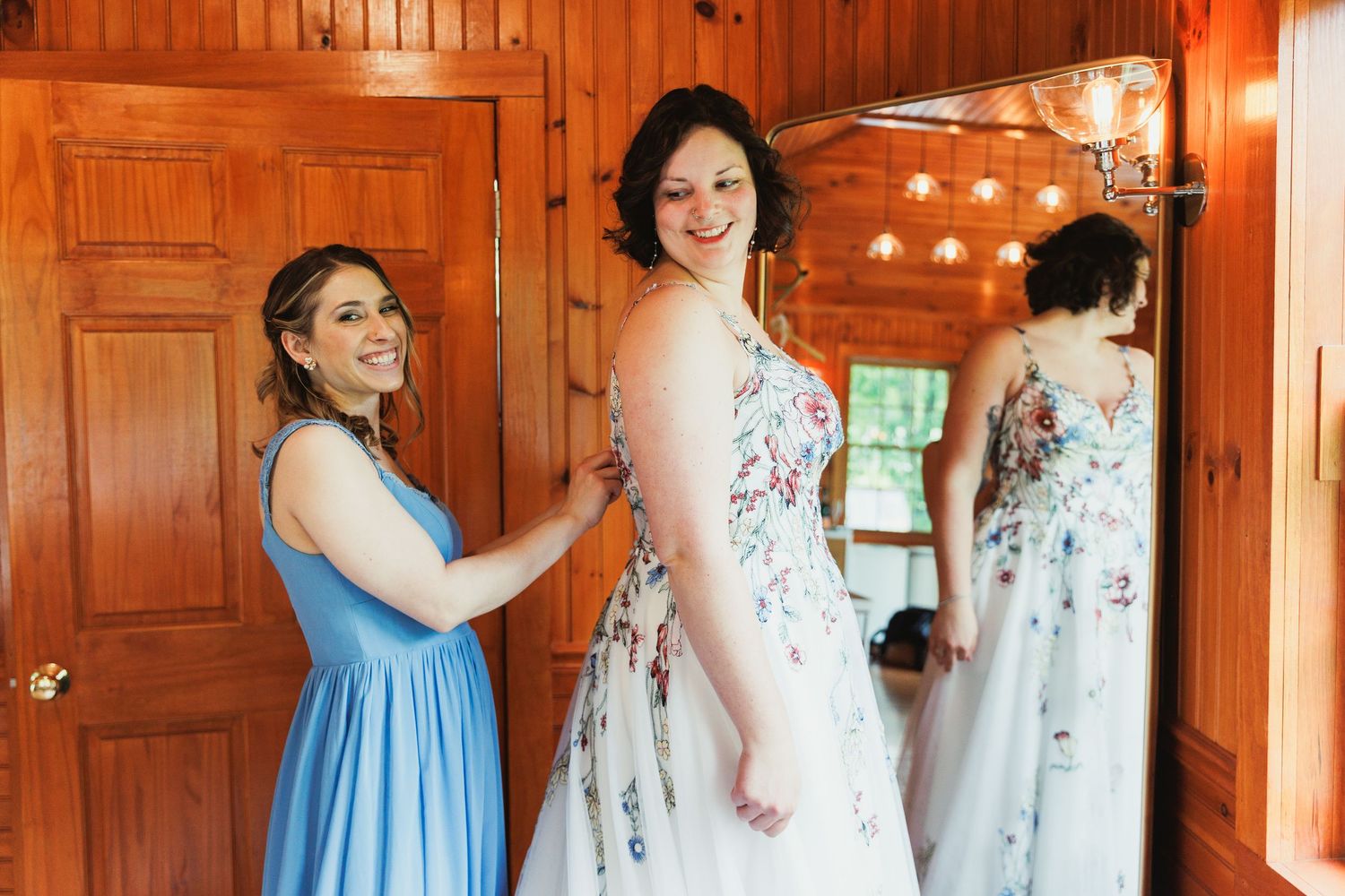 Bridesmaids in light blue dresses help with wedding preparations in a warm wood-paneled room.