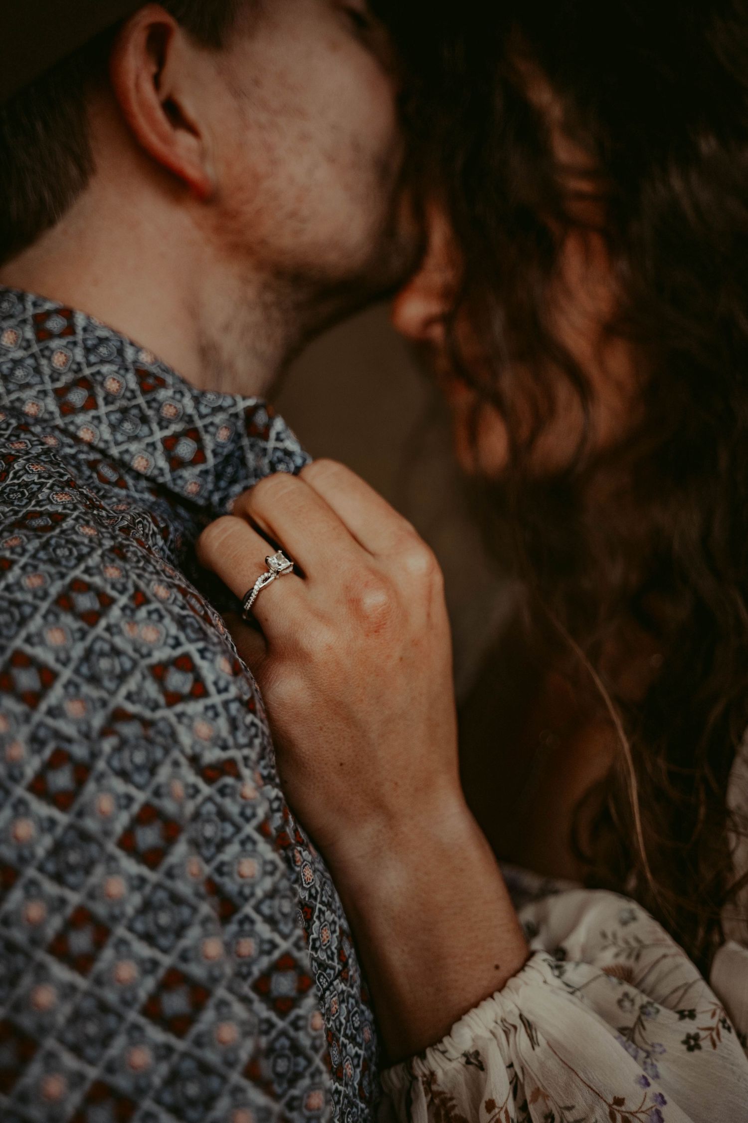 Close up shot of an engagement ring on hand with a patterned shirt in warm moody lighting.