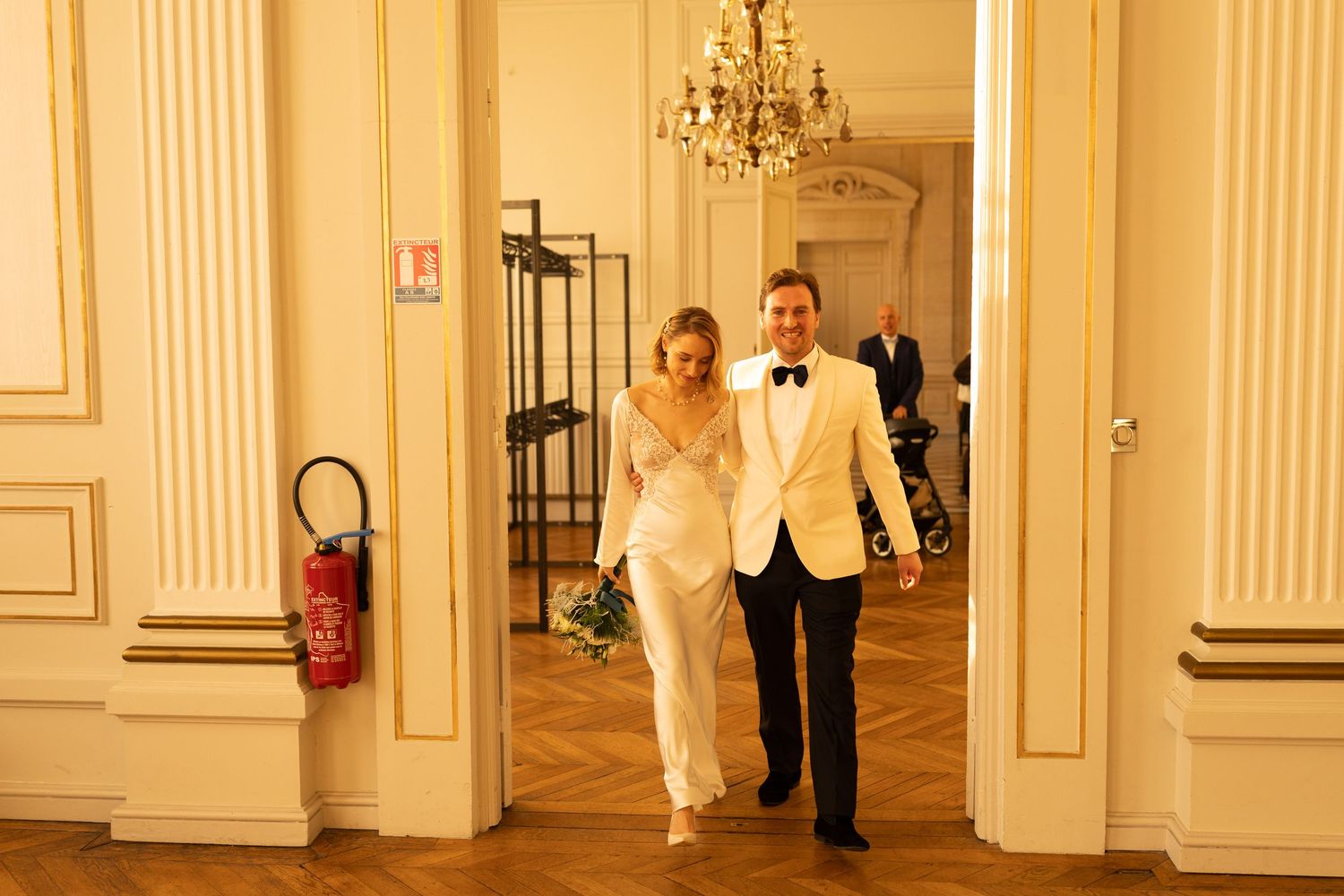 An elegant ballroom interior with white columns, crystal chandeliers, and hardwood floors in warm golden lighting.