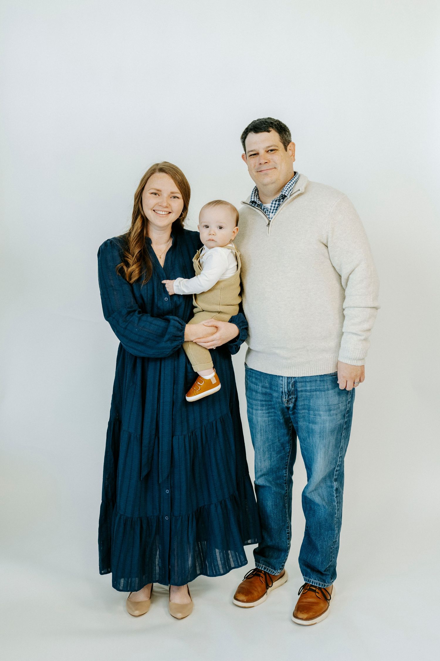 A family in coordinated navy and cream outfits poses together against a white backdrop in a minimalist studio setting.
