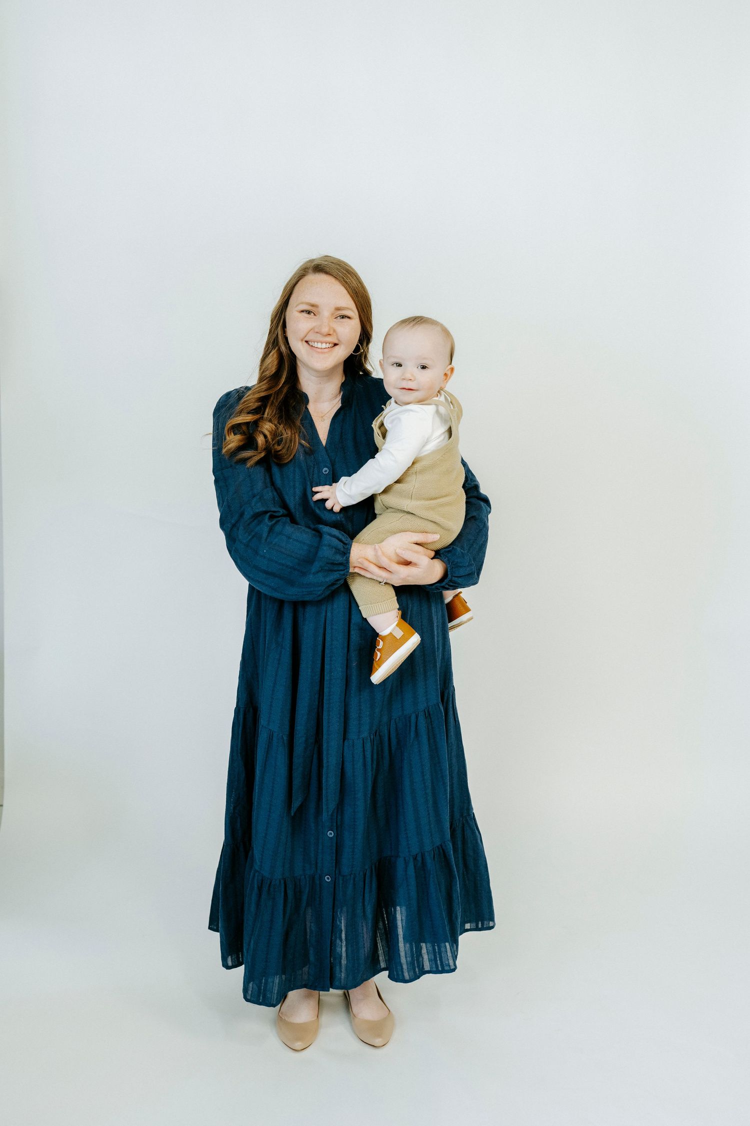 A navy blue tiered maxi dress creates an elegant silhouette against a light backdrop in this studio portrait.