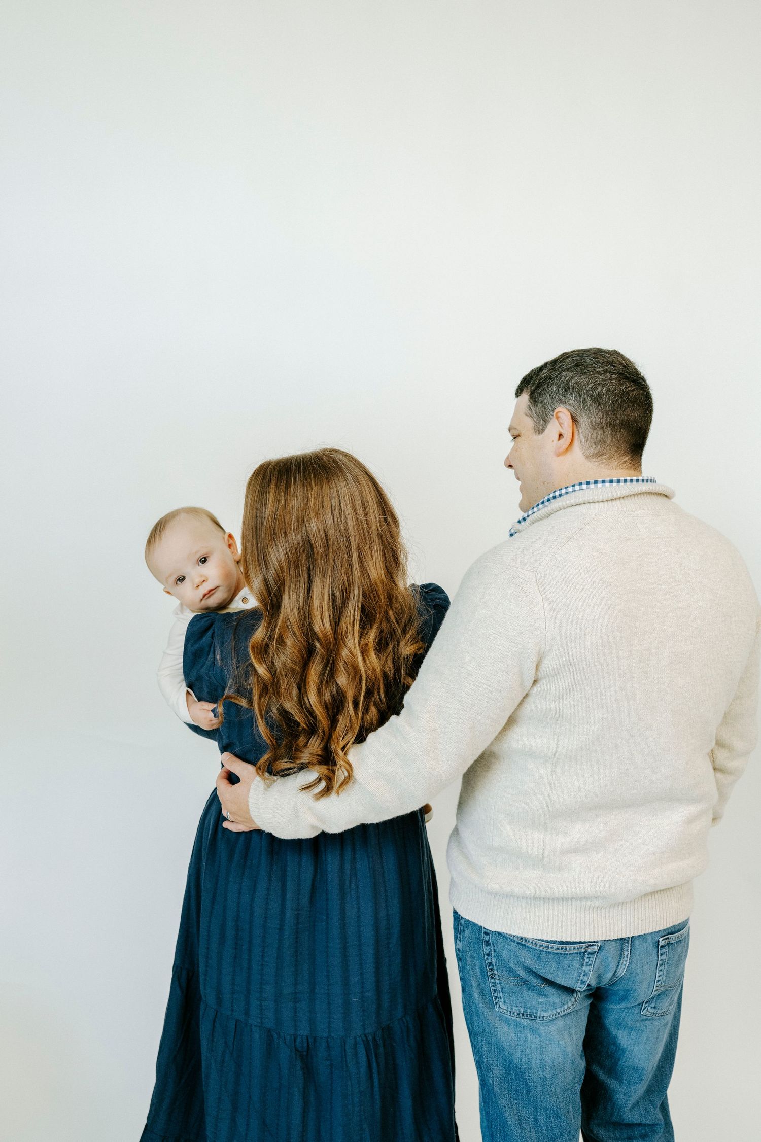 A series of four photos showing a couple in blue and cream colored outfits embracing from behind against a white backdrop.