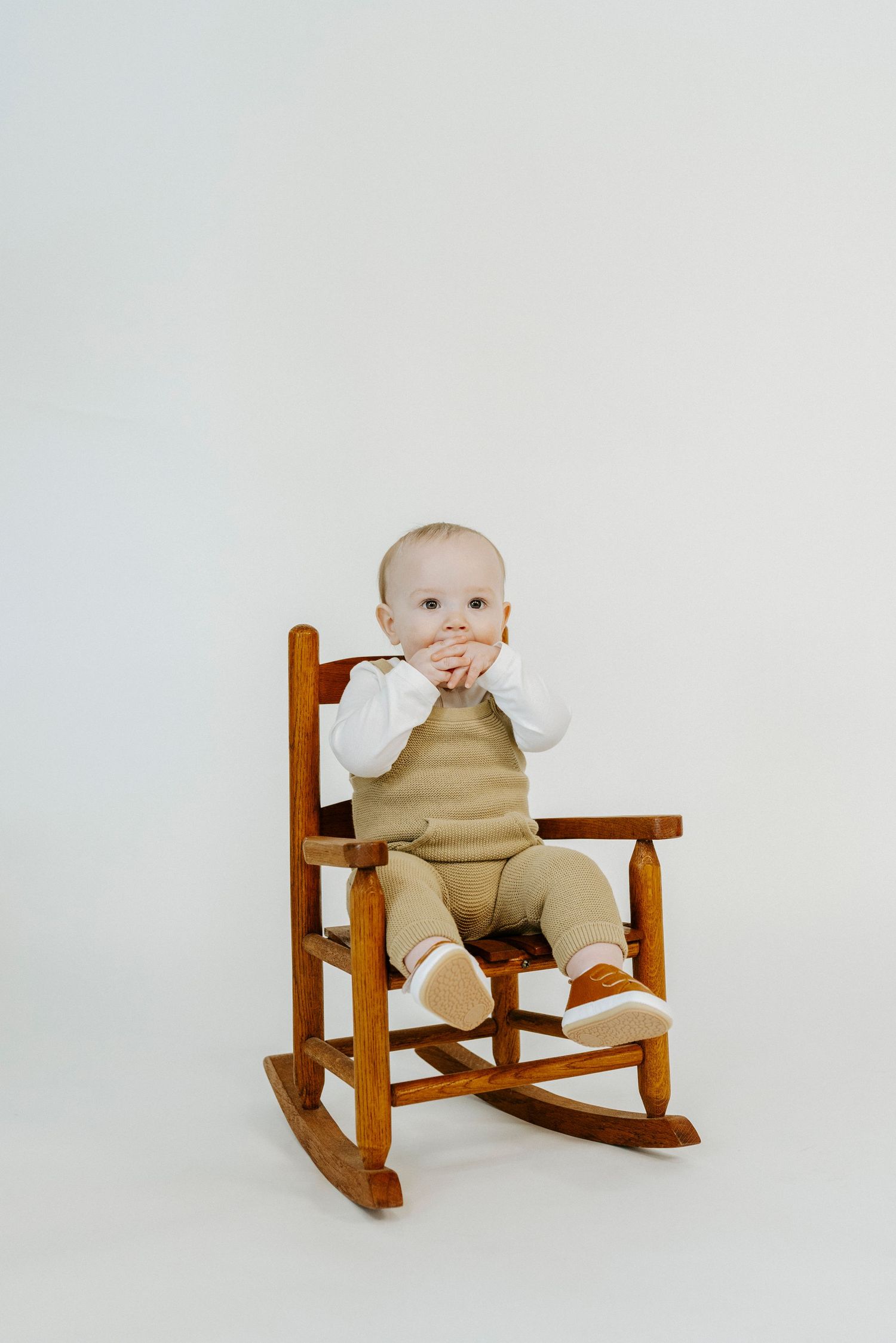 A small child in beige overalls sits in a wooden rocking chair against a white background in a series of photos.