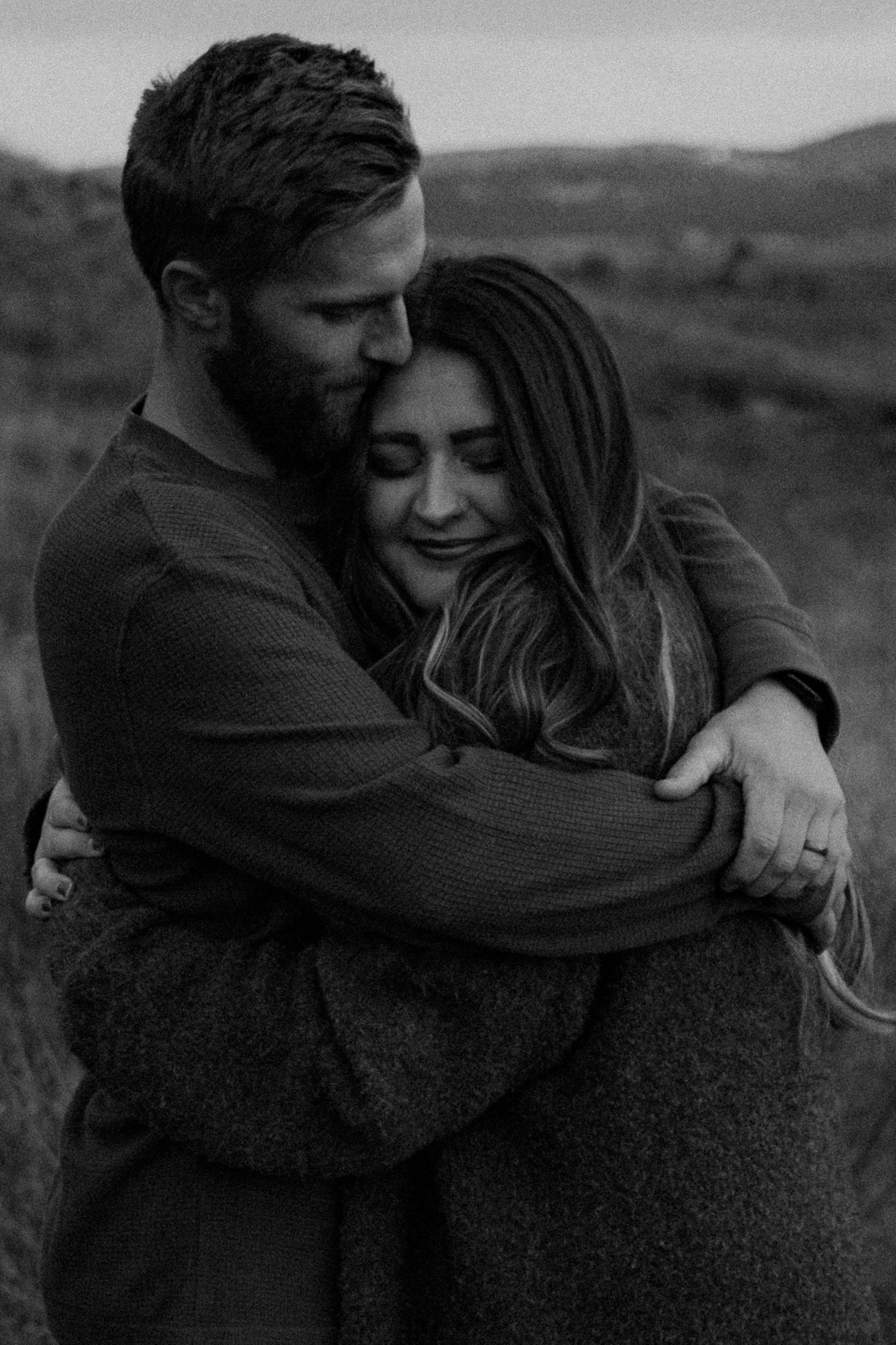 A couple shares an intimate embrace outdoors in a black and white photograph showing tender affection.