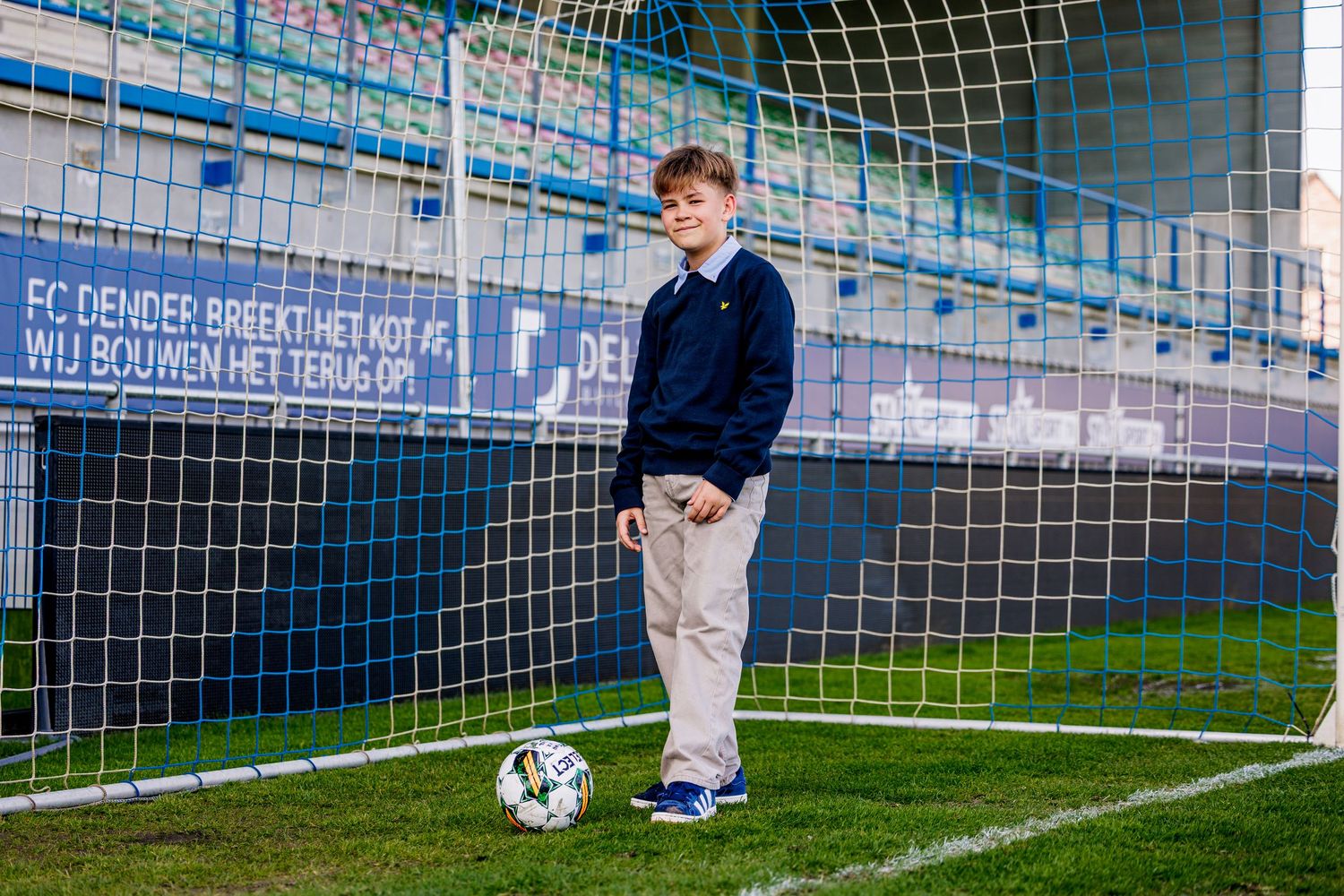 Soccer player practices penalty kicks on an empty field with goal nets visible in the background.