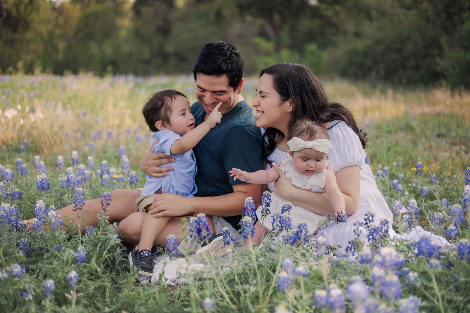 Family sitting together in a field of blooming bluebonnets during golden hour.