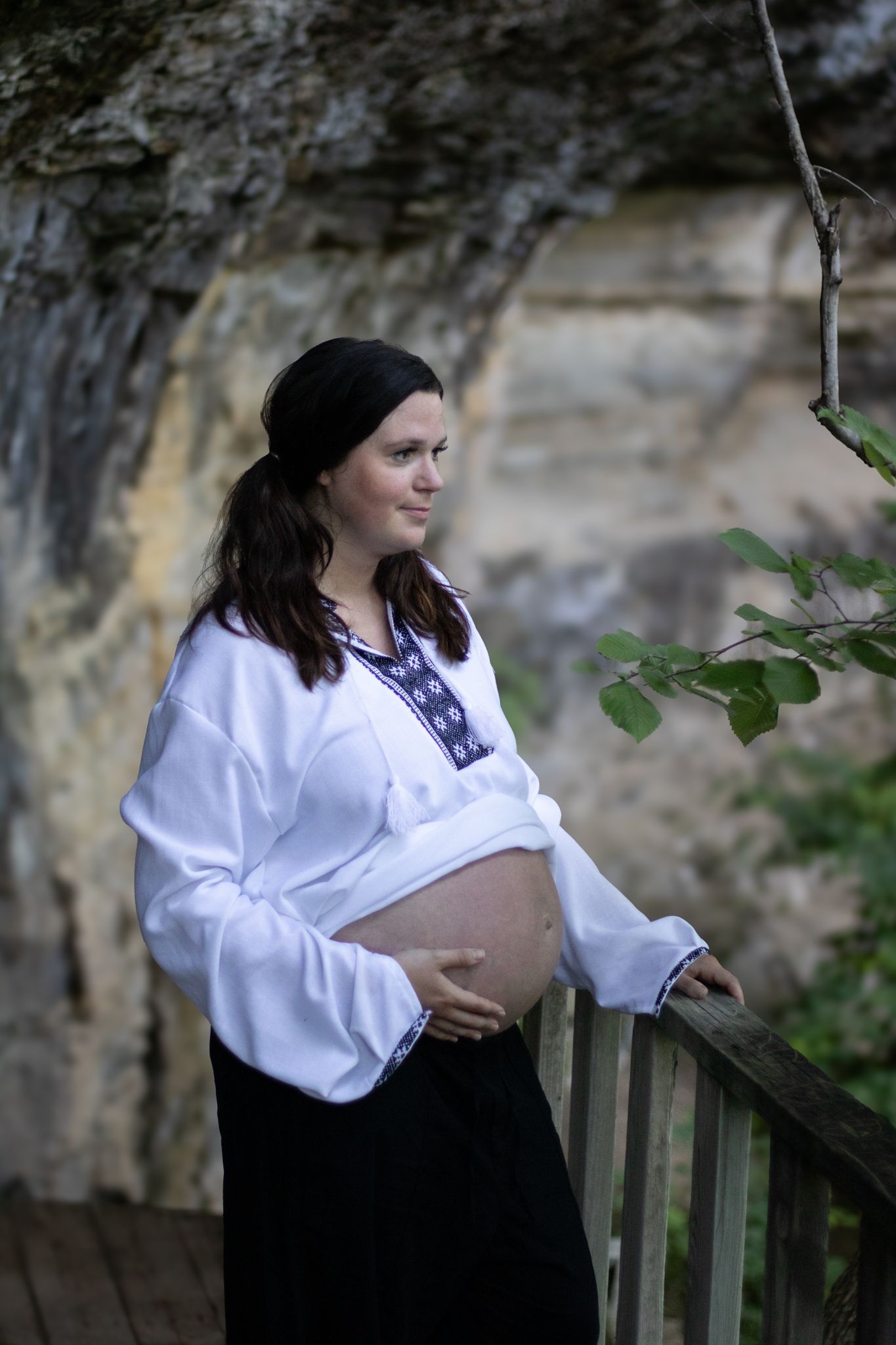 Woman holding her pregnant belly outside on a trail.