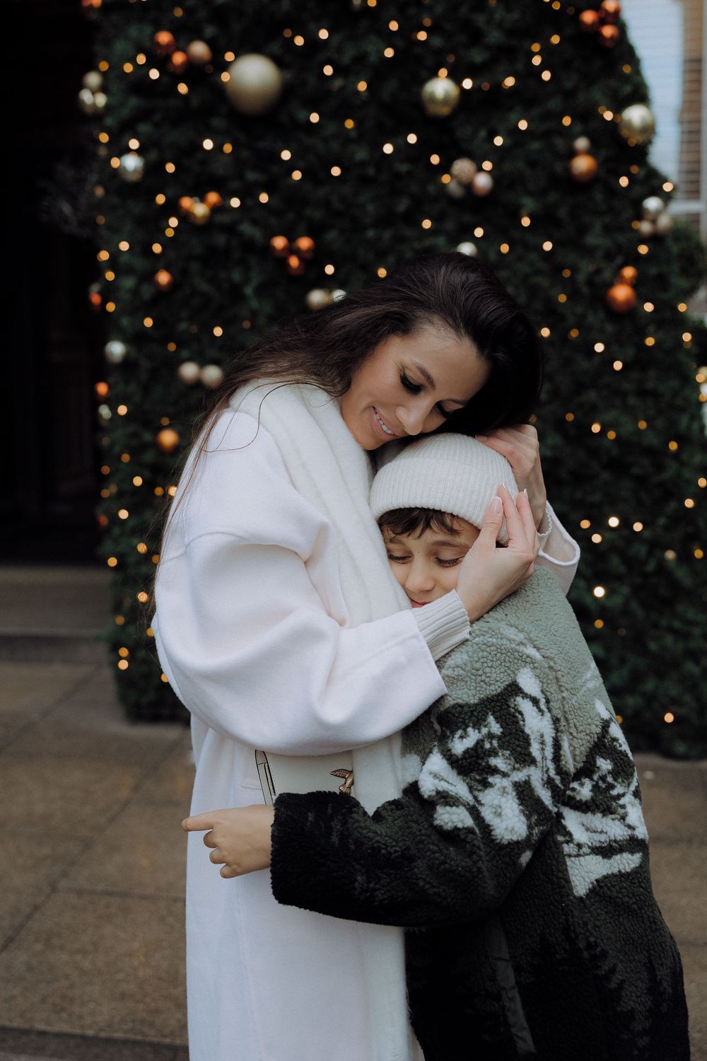 A tender holiday embrace in front of a decorated Christmas tree with glowing lights and ornaments.