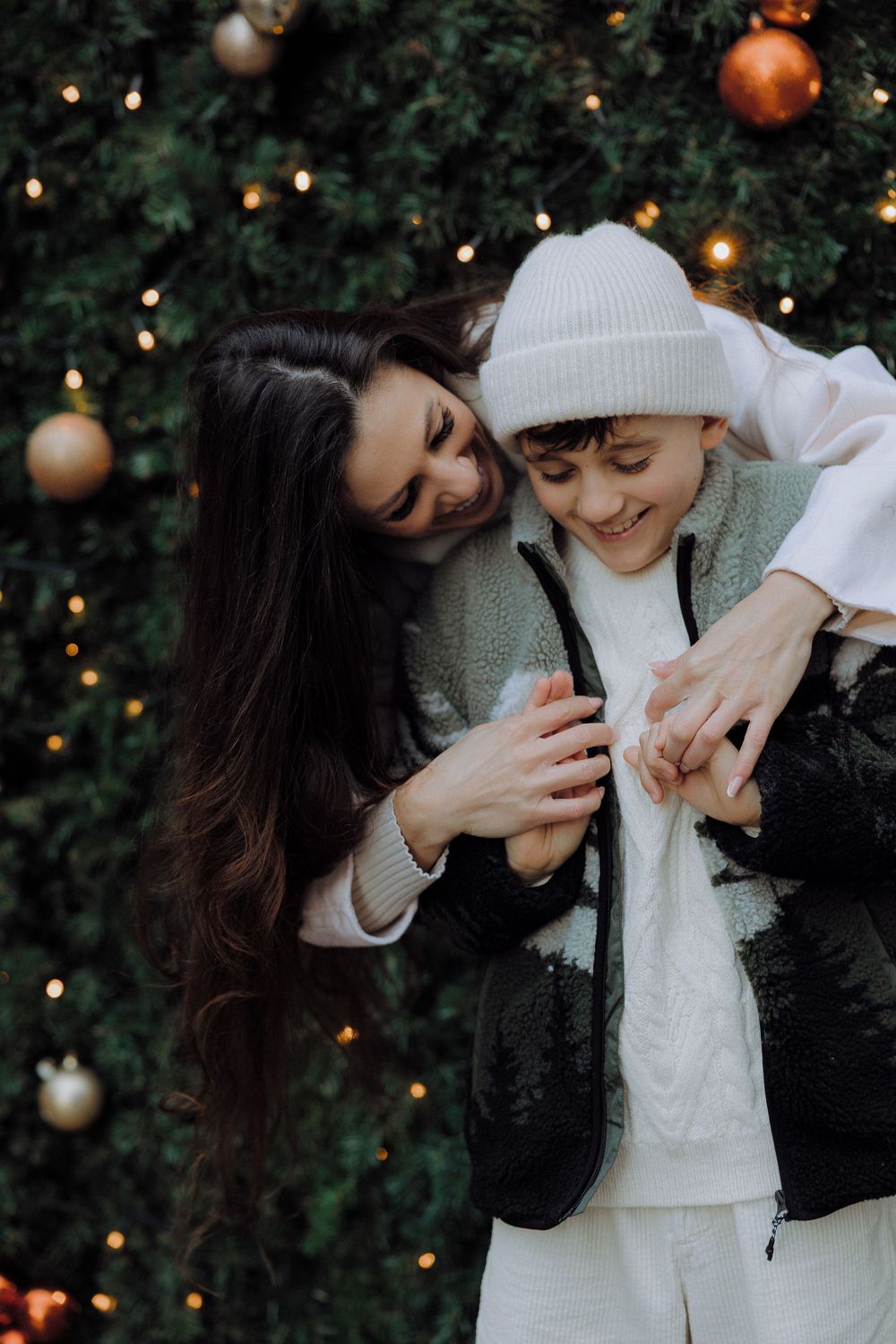 A couple shares intimate moments in front of a Christmas tree with twinkling lights and ornaments in the background.