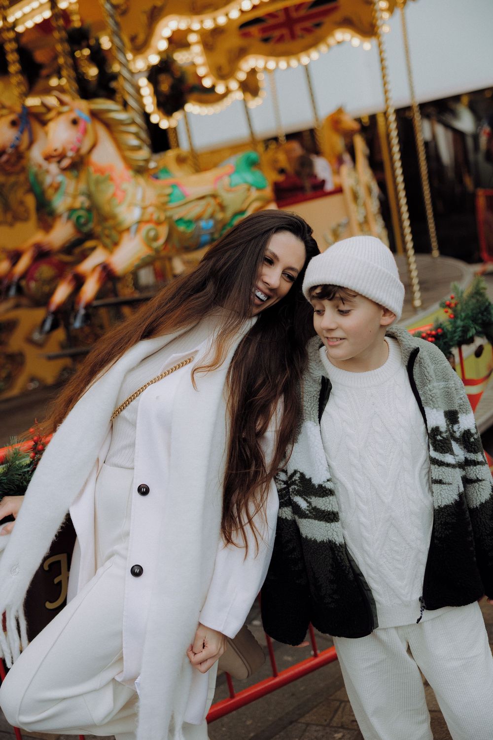 Festive winter scene with carousel lights and people dressed in all-white outfits.