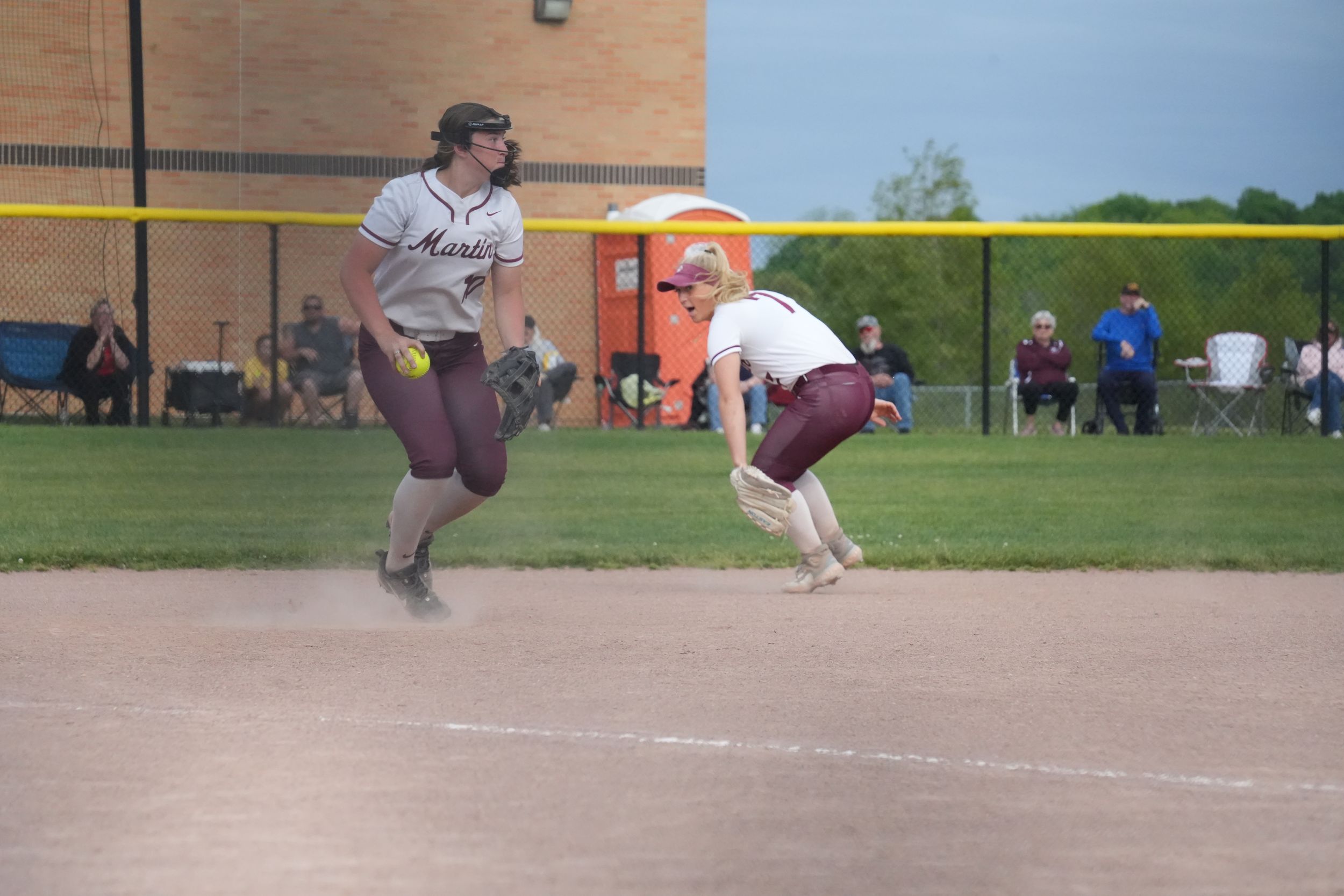 Two softball players in maroon uniforms near second base during a game on a dirt field.