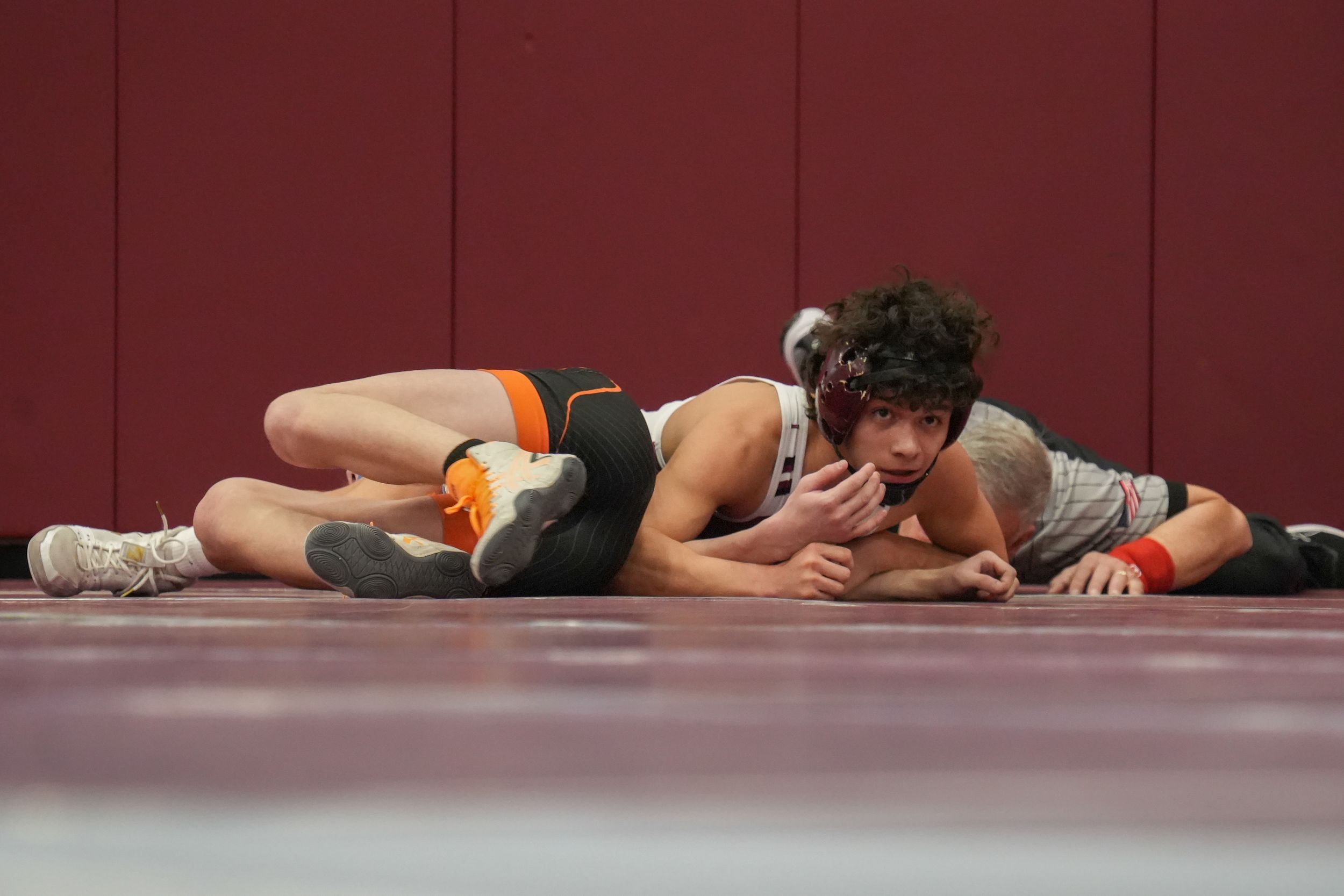 Two high school wrestlers compete on a mat, with one athlete pinning his opponent during an indoor wrestling match.