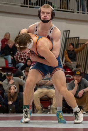 Two wrestlers compete in a high school wrestling match, one lifts his opponent during an intense takedown attempt.