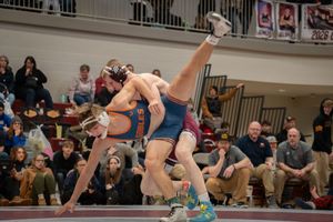 Two wrestlers compete intensely on a mat, one athlete lifted in the air during a high school wrestling tournament match.