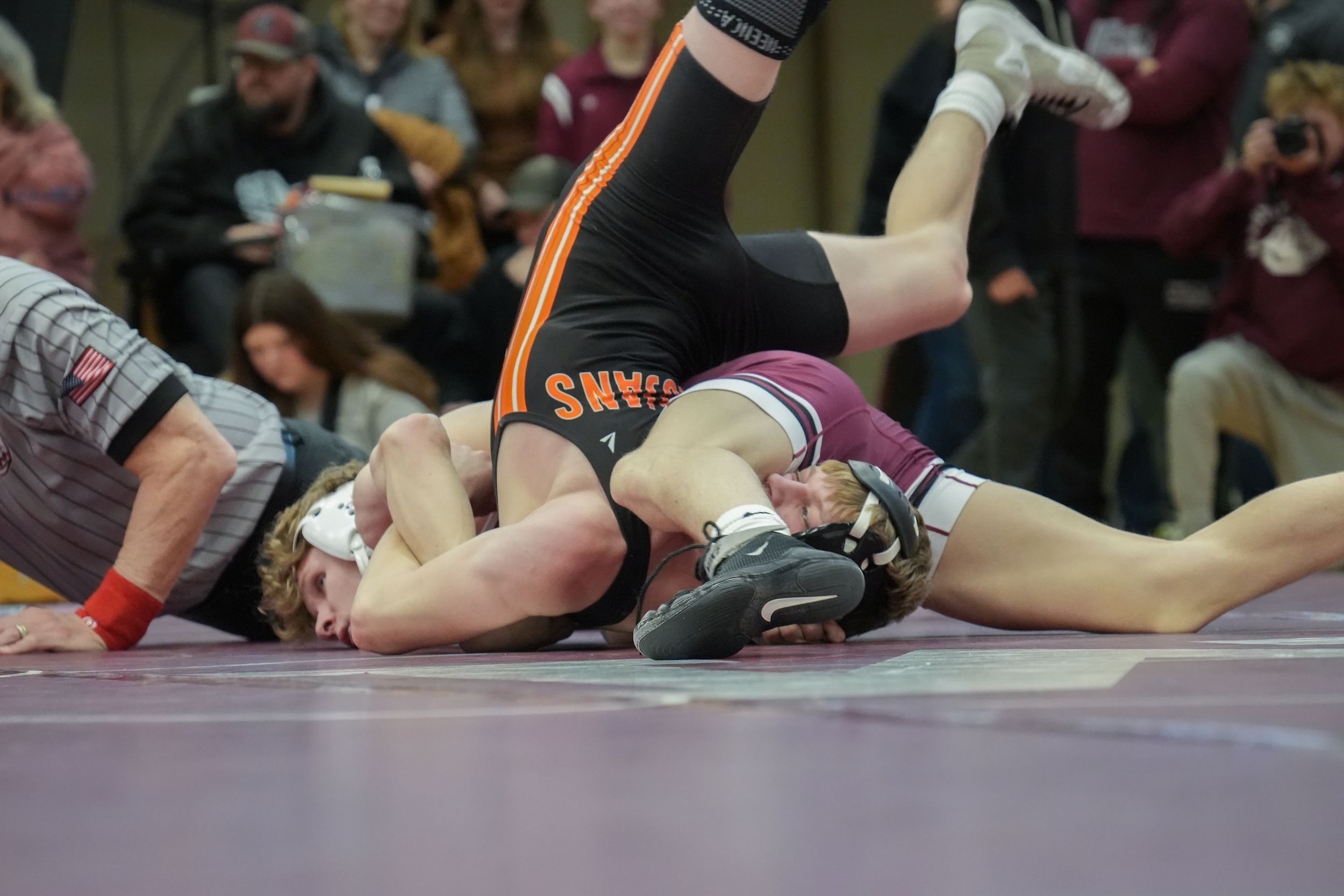 Two high school wrestlers compete on a mat, with one athlete executing a takedown move during a wrestling match.