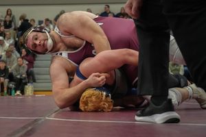 Two wrestlers compete on a mat, with one athlete in a dominant top position during an intense wrestling match.