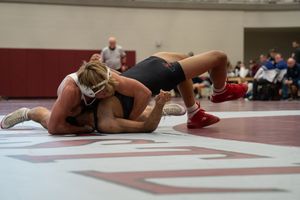 Two female wrestlers compete on a mat during an indoor wrestling match, with one athlete pinning the other down.