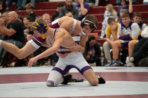 Two high school wrestlers compete on the mat during an intense wrestling match at a crowded gymnasium tournament.