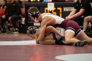 Two wrestlers compete on a mat during a high school wrestling match, with one athlete pinning the other down.