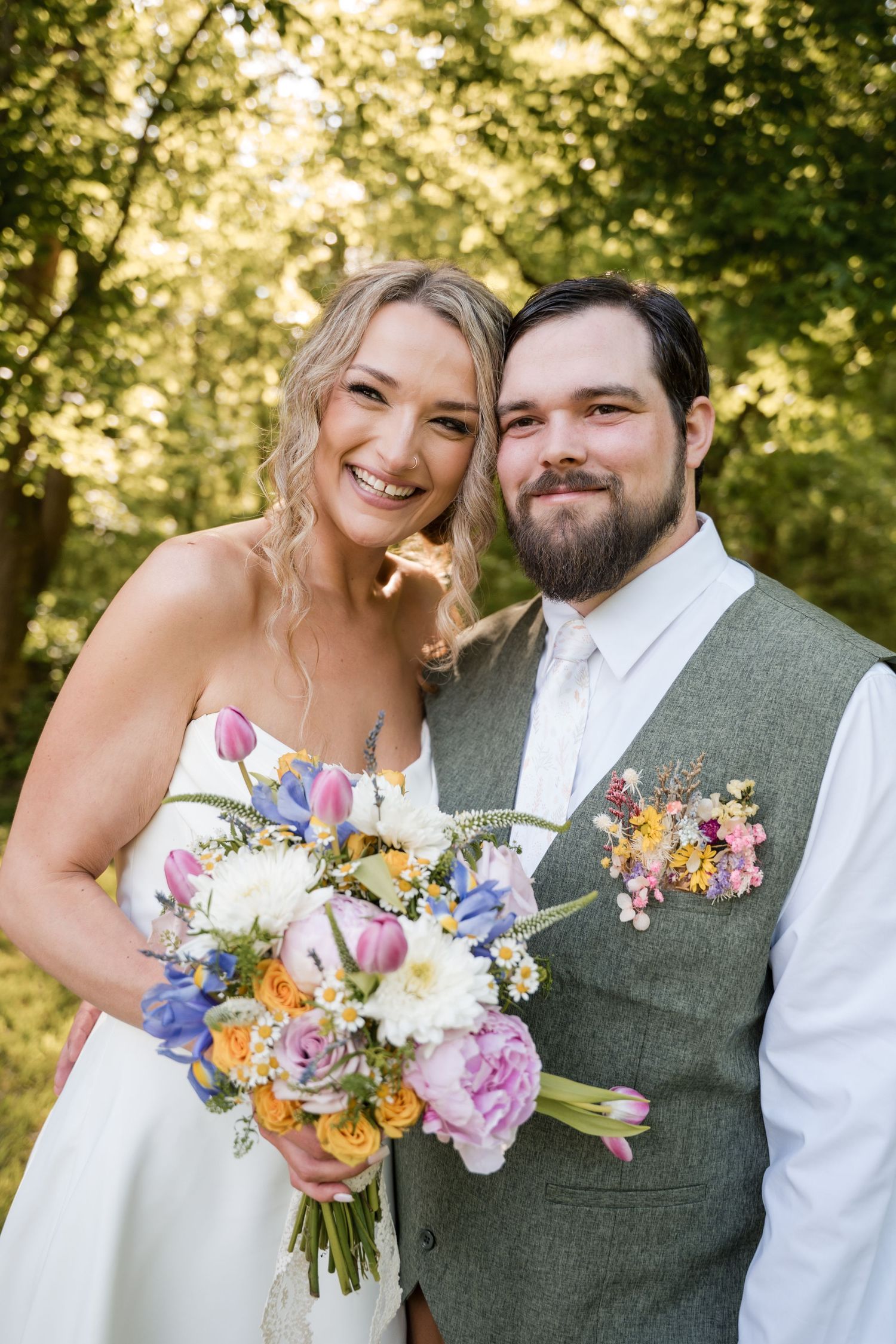 A happy couple celebrates their wedding day with a vibrant spring bouquet in a sunny outdoor setting.