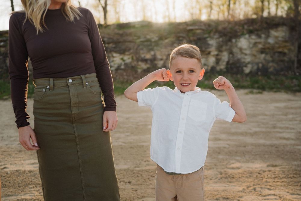 A child in a white button-down shirt and khaki pants poses outdoors next to someone wearing an olive skirt.