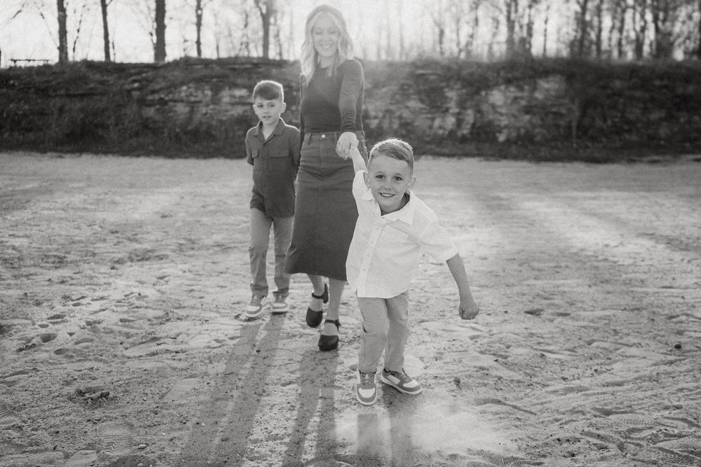 Black and white photo of children playing outside on a dirt path with a stone wall and trees in the background.