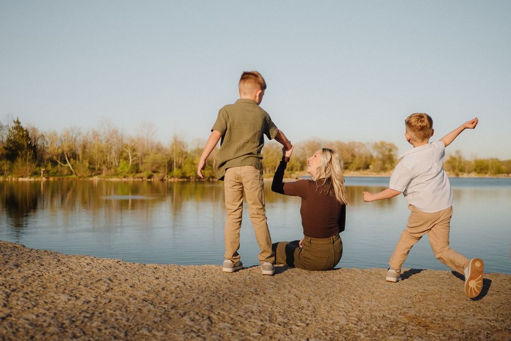 Family enjoying a sunset moment together by the lake shore with arms outstretched on a peaceful evening.