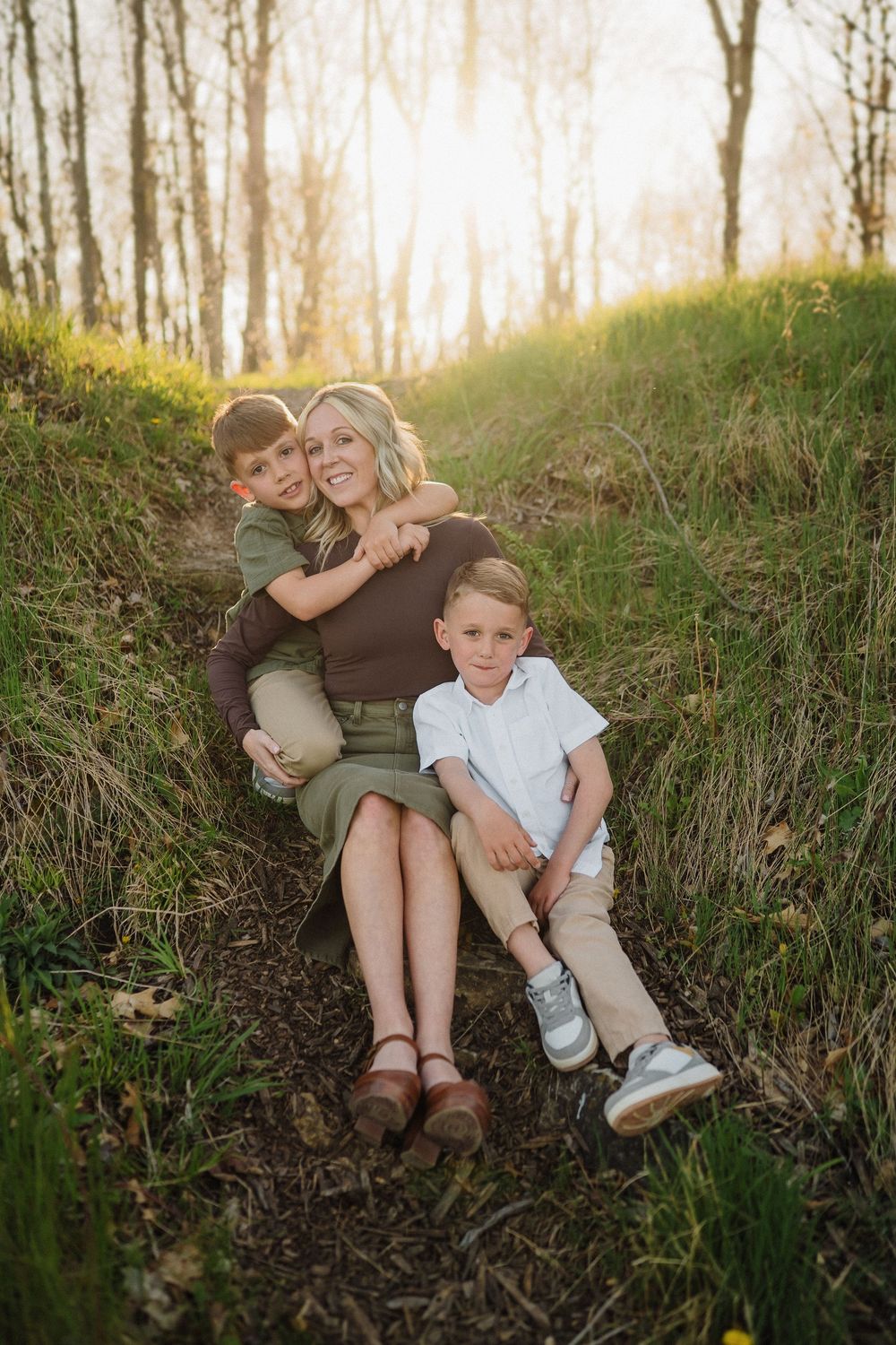 A family enjoying a sunny afternoon together sitting on a grassy hillside in the woods during golden hour.