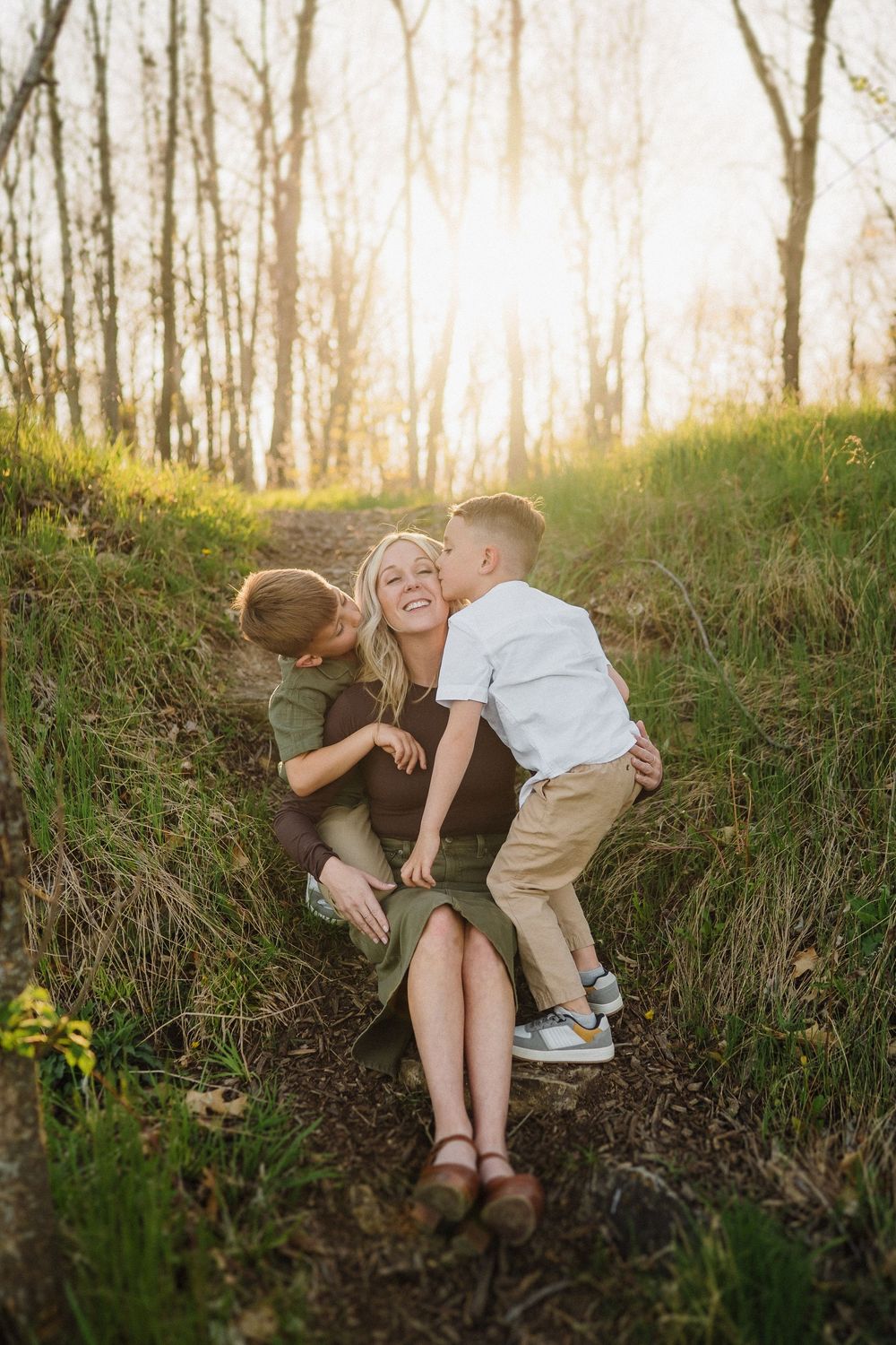 Family sharing a joyful moment together on a sunlit forest path during golden hour.