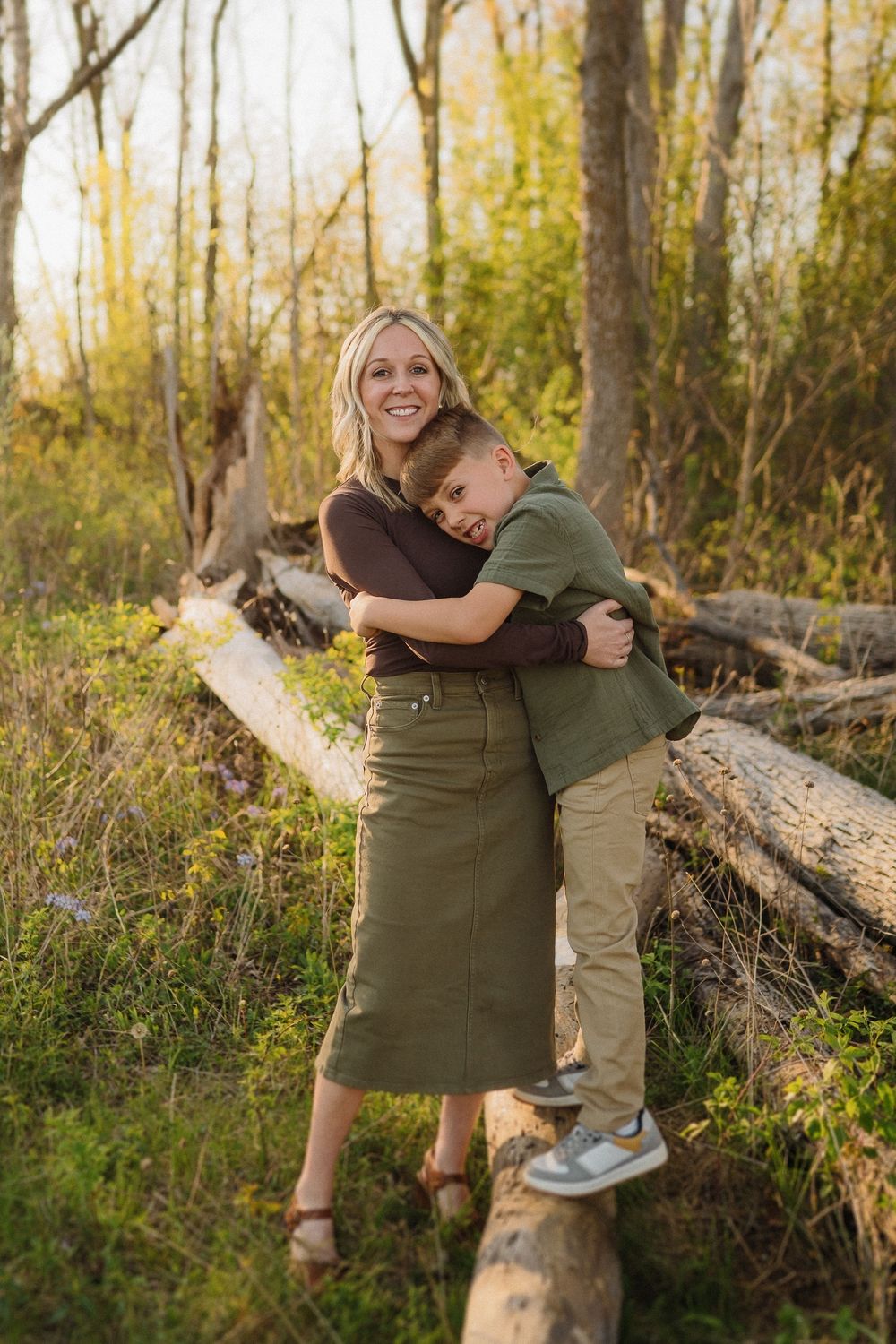 A warm embrace shared between parent and child while standing on a fallen log in an autumn forest setting.