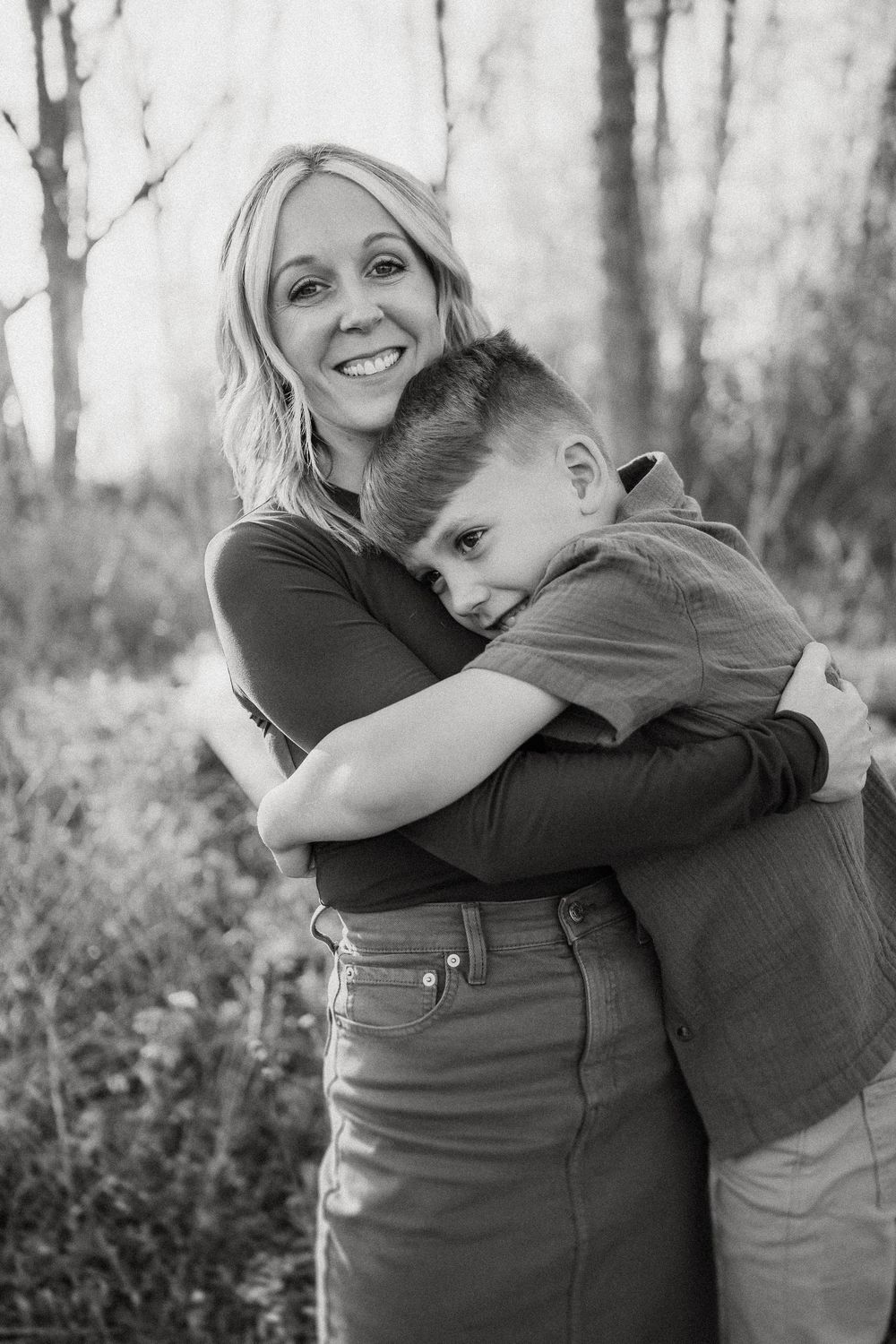 Black and white portrait capturing a tender moment of parent and child hugging in a wooded setting.