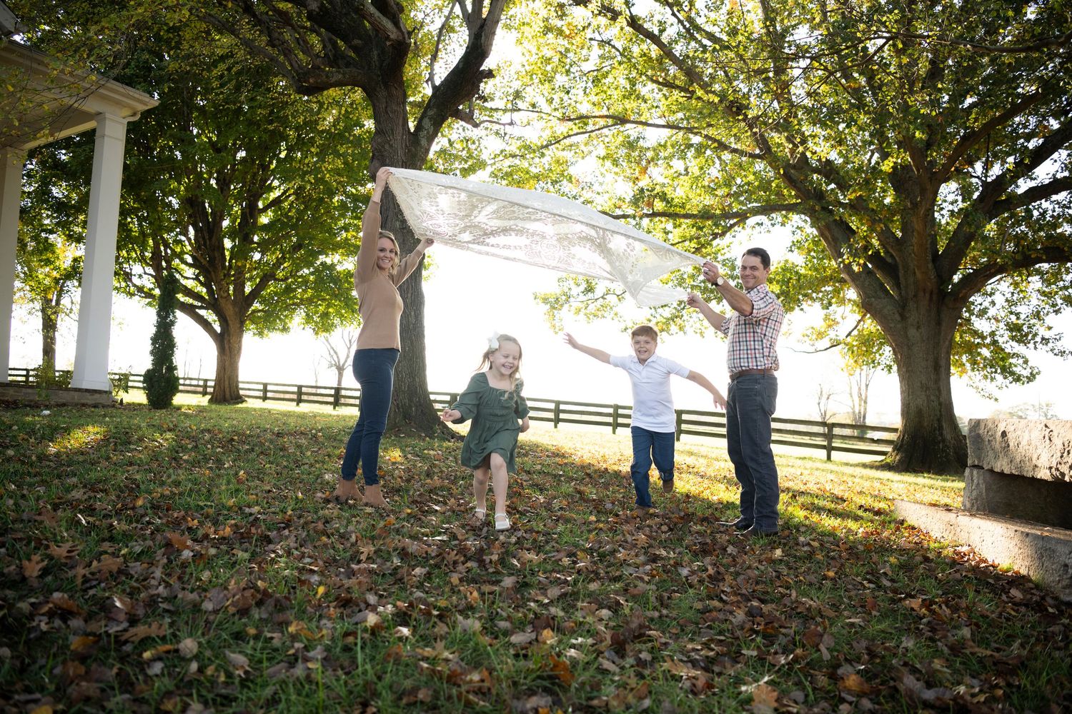 Family playing and jumping together in a leaf-covered yard during golden hour for their family photos  in Columbia, TN at Muletown Farm.