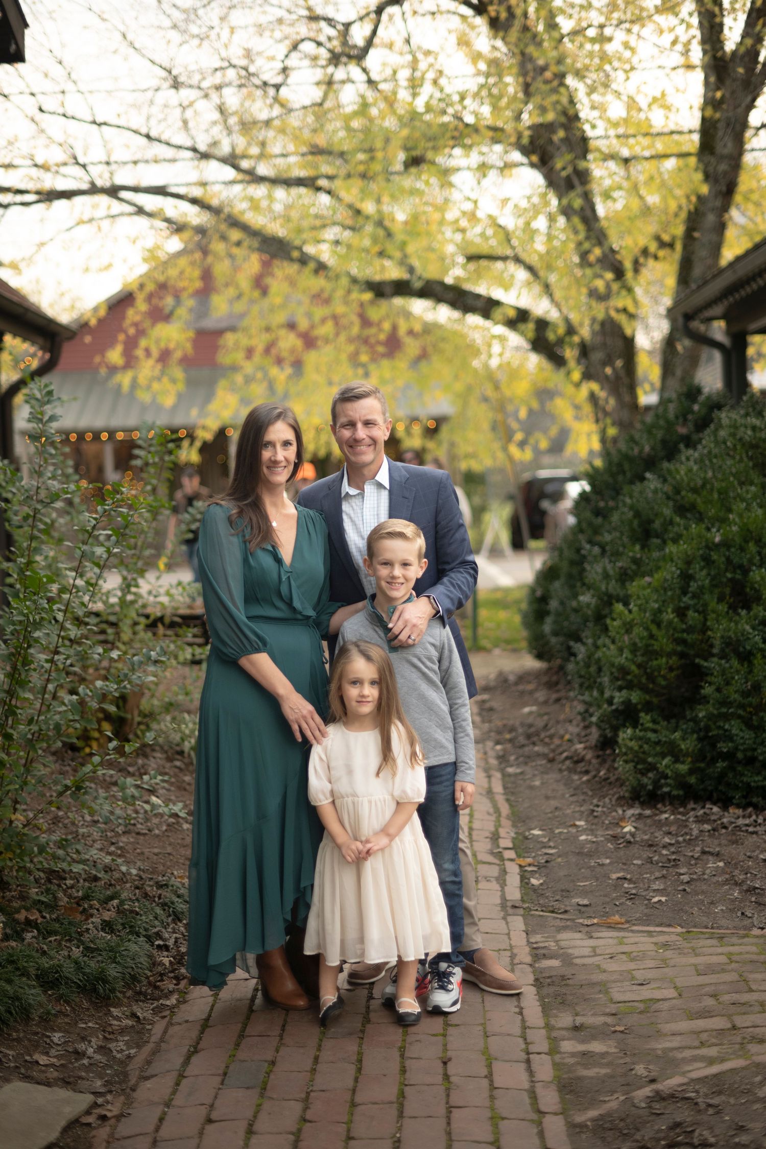 Family portraits poses for portraits on brick pathway with fall foliage in background in Leiper's Fork.