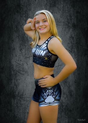 Cheerleader poses in sparkly black uniform against textured dark background.
