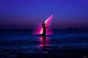Silhouetted figure stands on paddleboard against vibrant pink and purple sunset over calm ocean waters.