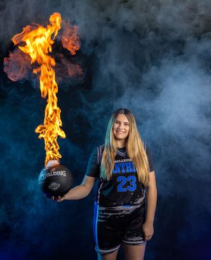 Basketball player poses in uniform with flaming basketball against dramatic blue smoke background.