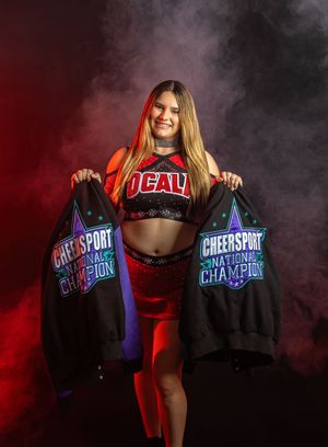 An athlete in red athletic wear displays two championship banners in a moody studio setting with dramatic smoke effects.