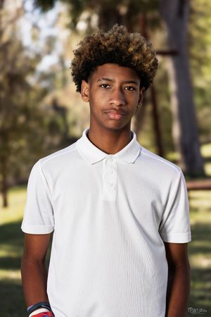 Portrait of person wearing a white polo shirt in an outdoor setting with trees in the background.