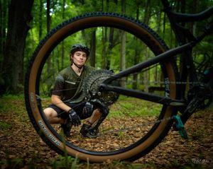 A mountain biker poses with a bicycle wheel in a lush forest setting.