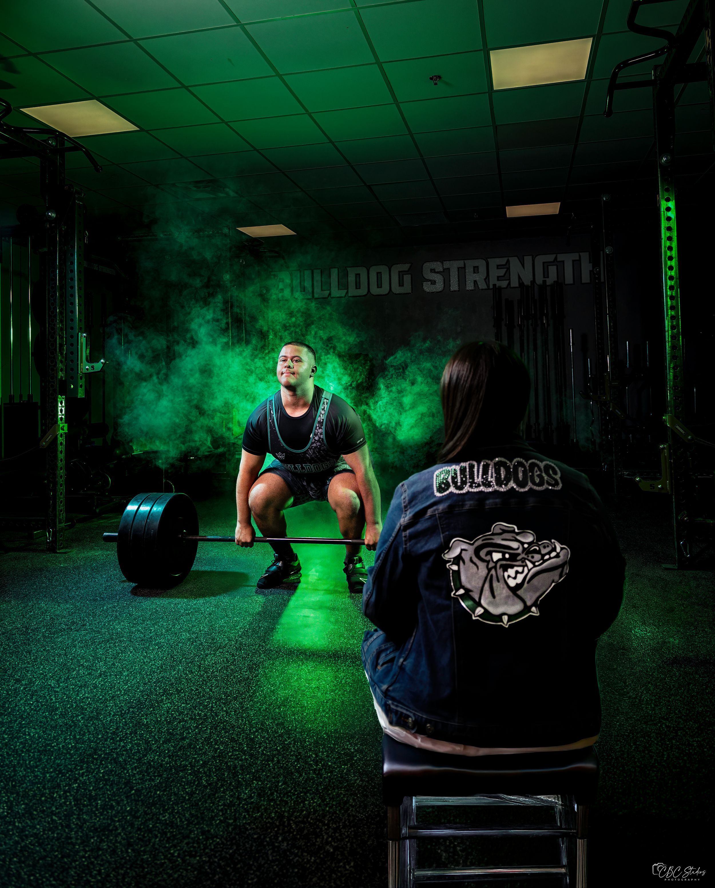 Weightlifter performs deadlift exercise in dark gym with dramatic green smoke effects creating moody atmosphere.