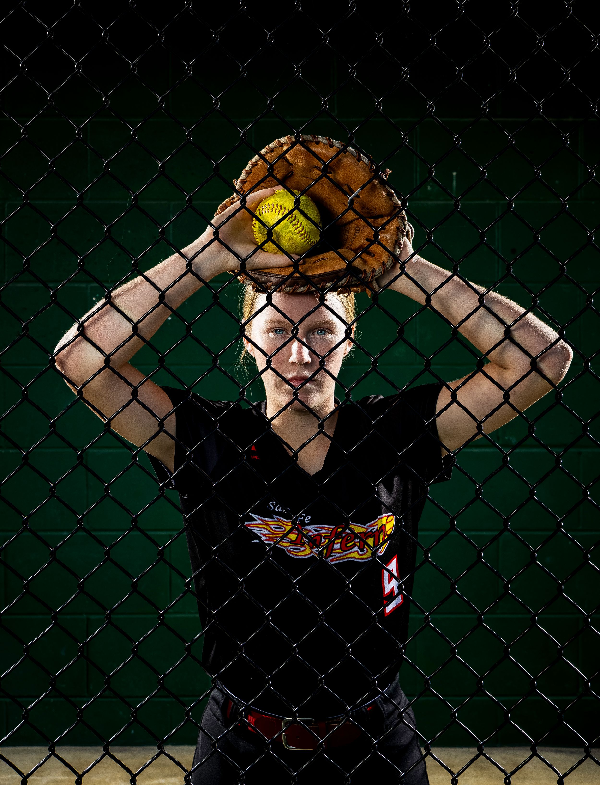 A person in black clothing poses against a chain link fence in a sequence of connected action shots.